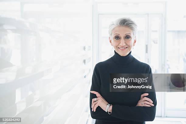 mature businesswoman wearing black sweater in modern office - black polo shirt stock pictures, royalty-free photos & images