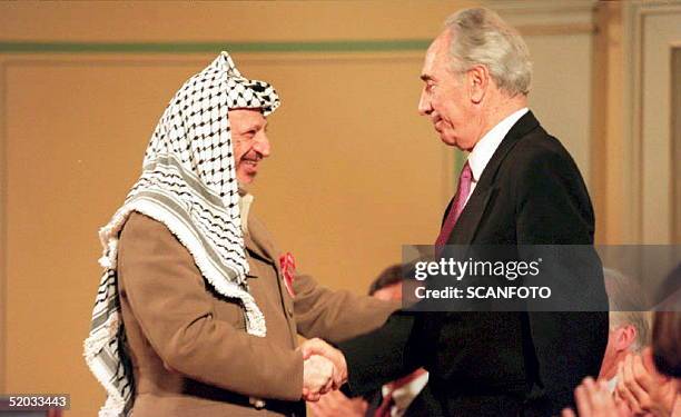 Chariman Yasser Arafat shakes hands with Israeli Foreign Minister Shimon Peres 18 May 1994 at a ceremony honoring Norway's role in the Israeli-PLO...
