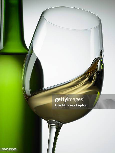 white wine swirling in glass with green wine bottle - bottle white wine stock-fotos und bilder