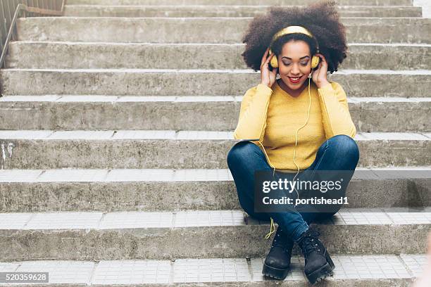 souriante jeune femme avec un casque assis sur les escaliers jaune - mannequin mode street photos et images de collection