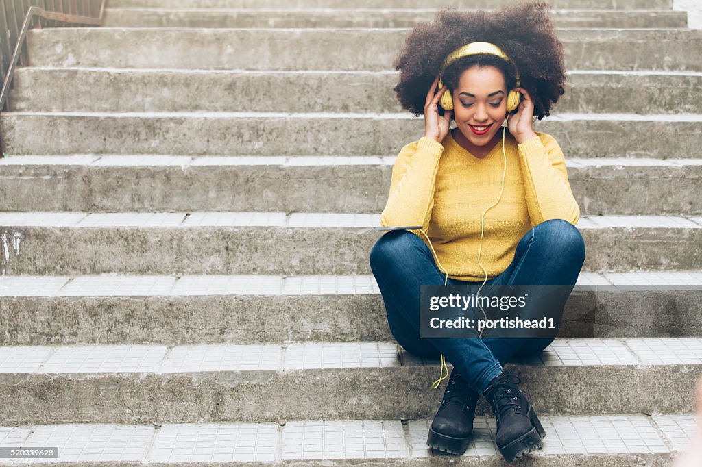 Smiling young woman with yellow headphones sitting on stairs
