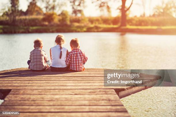 kids sitting at the pier. - three people sitting stock pictures, royalty-free photos & images