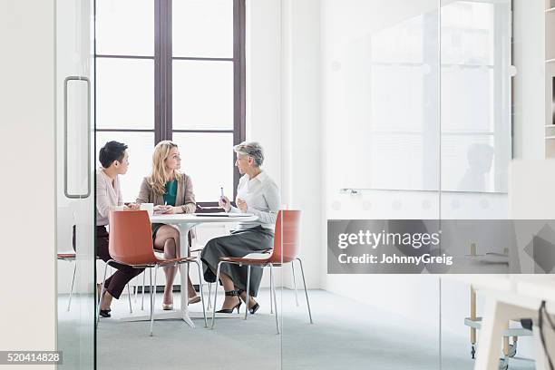 drei frauen sitzen auf tisch in modernen büro - business people having meeting in modern office stock-fotos und bilder