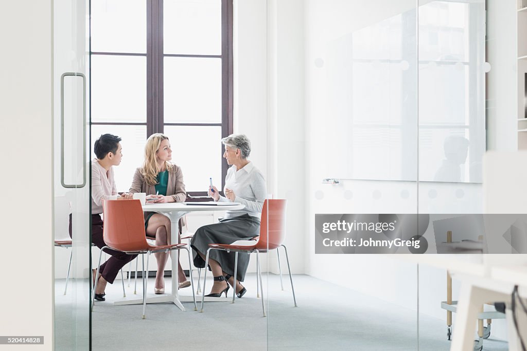 Tres mujeres sentado en la mesa en oficina moderna
