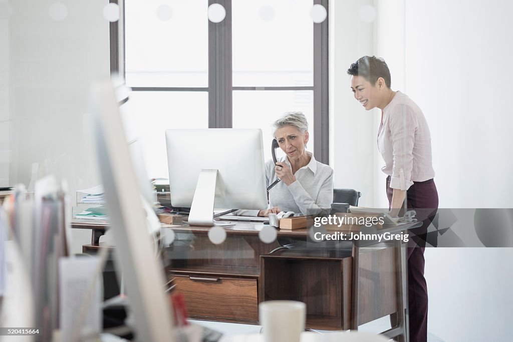 Mature woman at desk on phone with female colleague