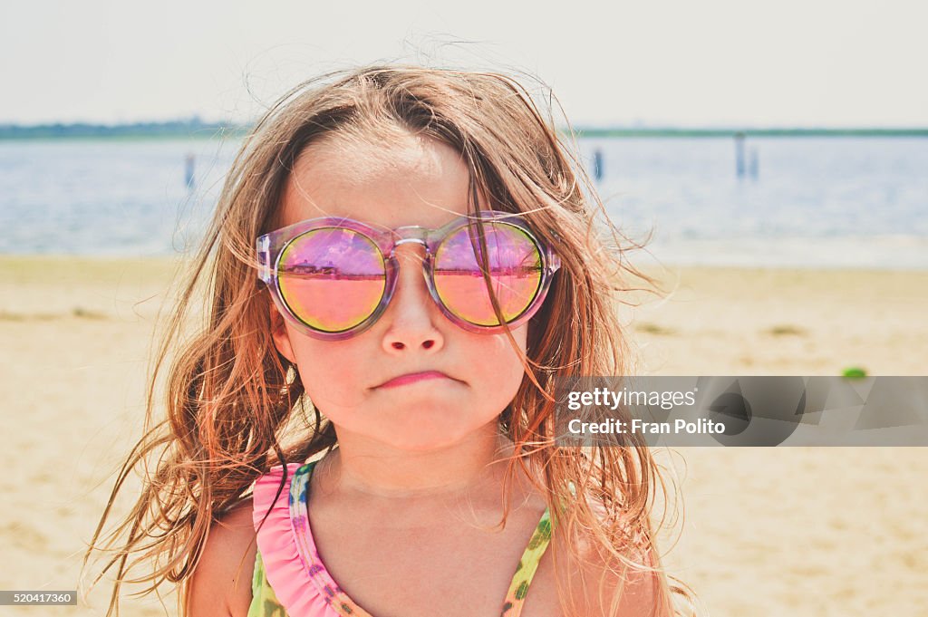 Young girl at the beach wearing sunglasses.