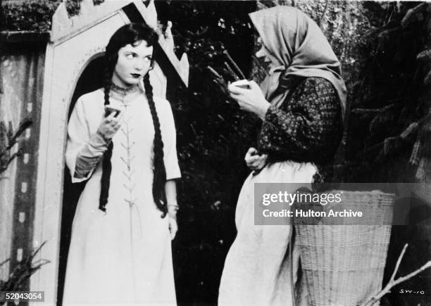 Half an apple in her hand, German actress Elke Arendt , as Snow White, gazes warily at fellow German actress Addi Adametz, as the Evil Queen...
