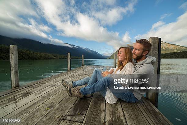 young couple relaxes on lake pier, morning sunlight - nelson lakes national park stock pictures, royalty-free photos & images