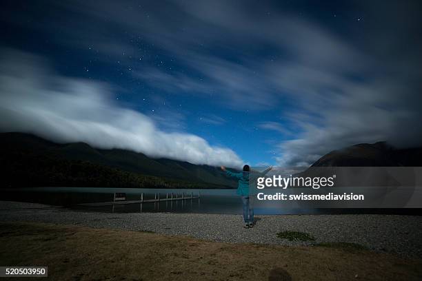 woman stands on lake shore at night, arms outstretched - nelson lakes national park stock pictures, royalty-free photos & images