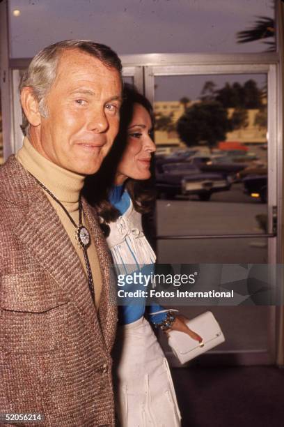 American talk show host and comedian Johnny Carson wears a turtleneck shirt and bolo tie as he walks with his third wife Joanna Holland, May 1972.