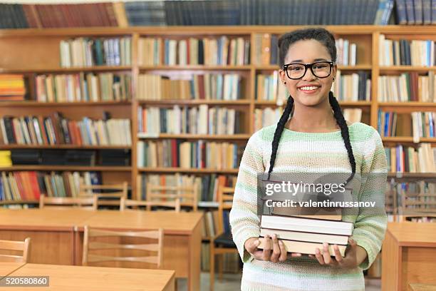 attractive young woman holding stack of books in the library - college preparation stock pictures, royalty-free photos & images