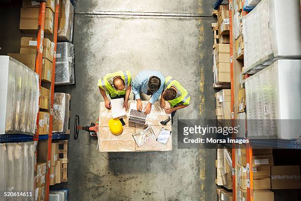 supervisor using laptop with workers at warehouse - overhead view stock-fotos und bilder