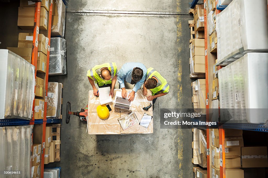 Supervisor using laptop with workers at warehouse