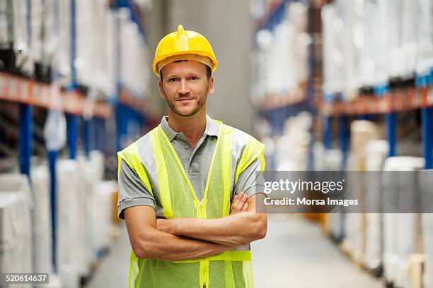 confident worker standing in warehouse - protection helmet stock-fotos und bilder