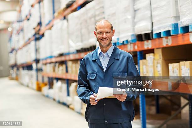 happy worker standing in warehouse - overalls stock-fotos und bilder