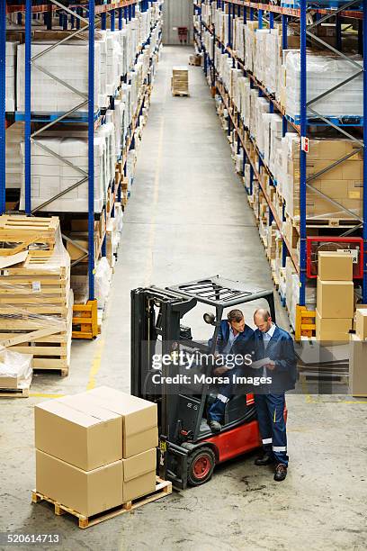 Workers On Forklift Discussing At Warehouse High-Res Stock Photo