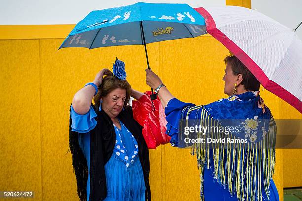 Women wearing traditional Sevillana dresses hold umbrellas as they arrive to the Feria de Abril under a heavy rain on April 12, 2016 in Seville,...