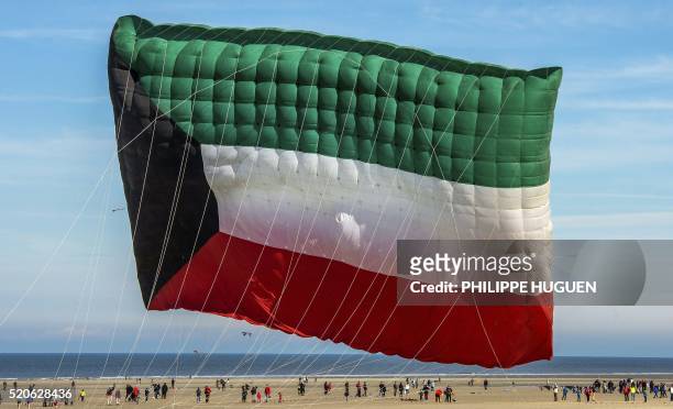 People fly a kite in the shape of the Kuwaiti flag during the 30th International Kite Festival in Berck-sur-Mer in northern France on April 12, 2016.