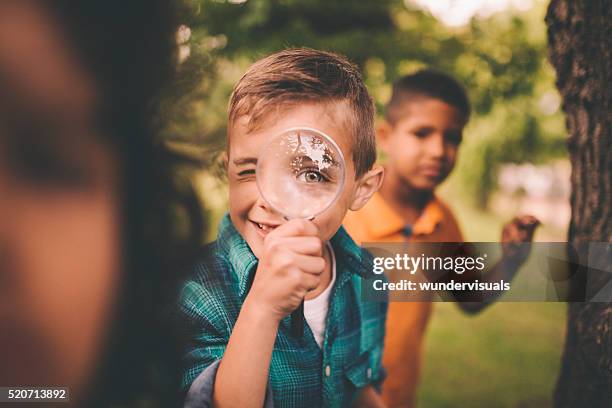 chico en parque sosteniendo un lupa un su ojo - lupa fotografías e imágenes de stock