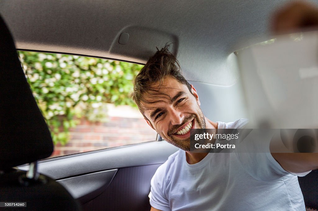 Happy man taking selfie on mobile phone in car