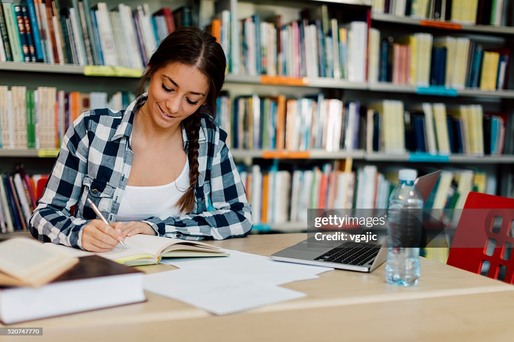 Female student using laptop for taking notes to study.