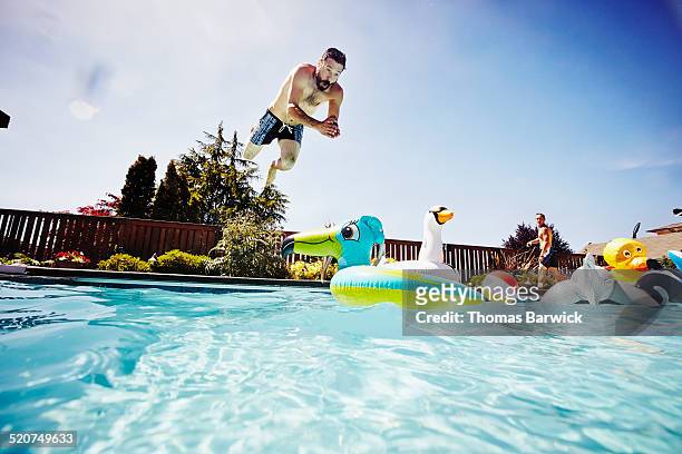 man diving from pool deck towards pool toy - jump in pool stockfoto's en -beelden
