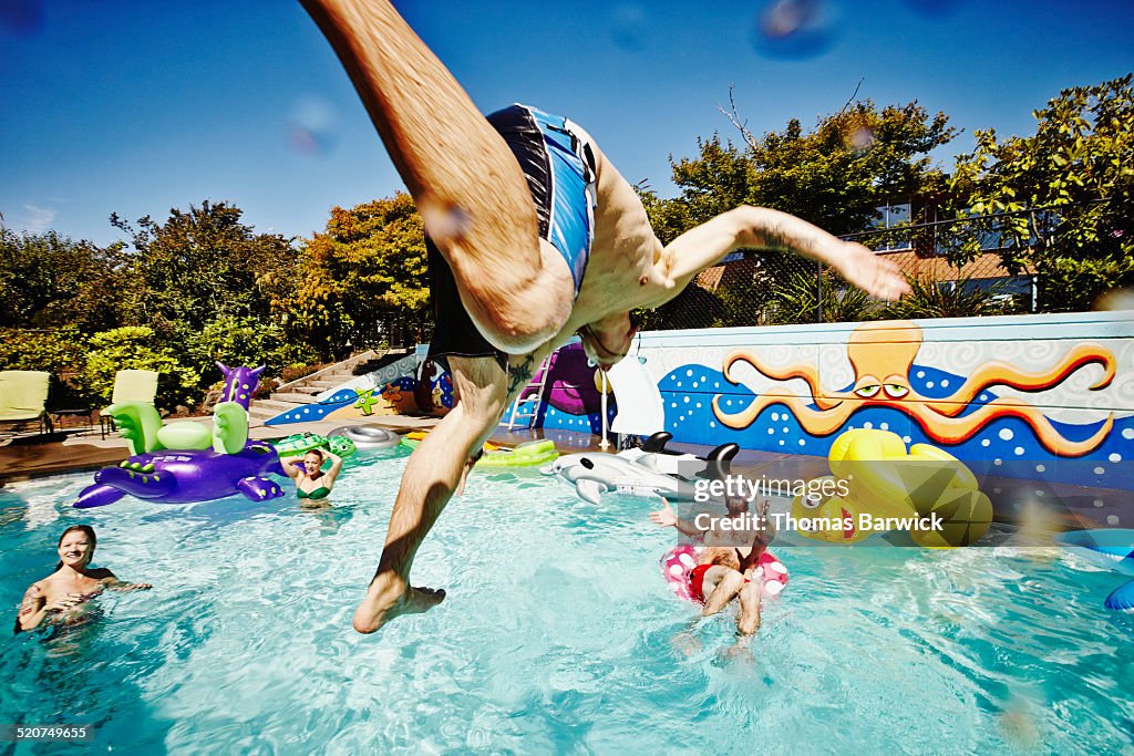 Man in mid air jumping into pool during party