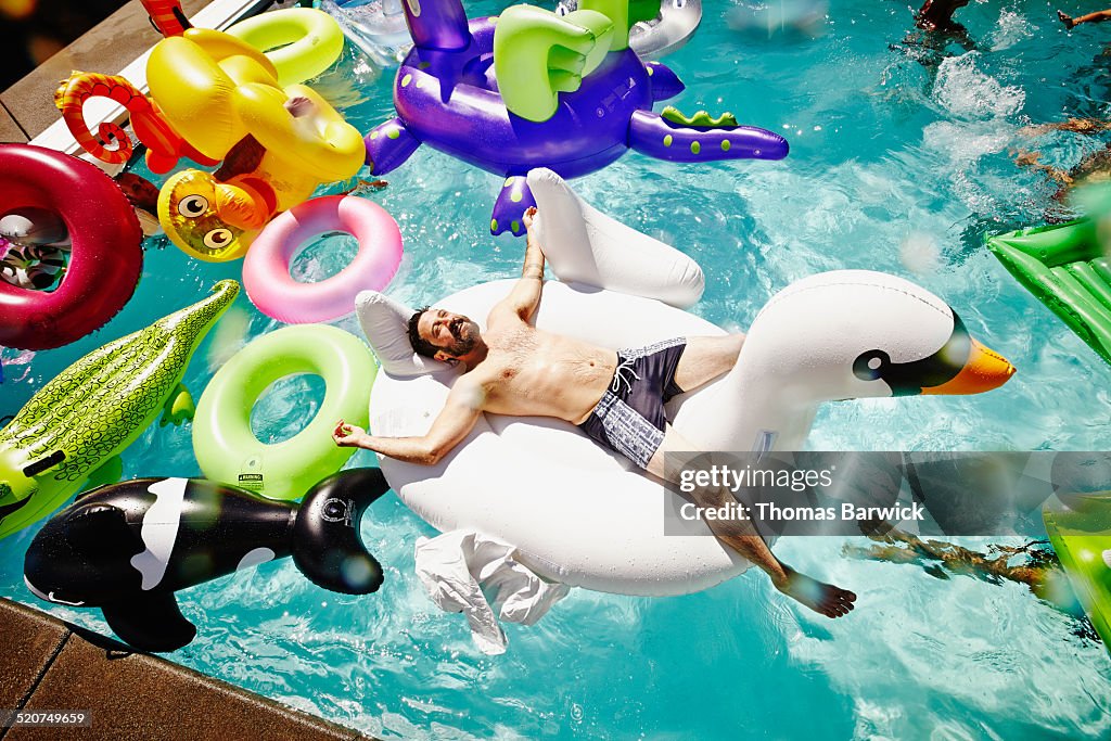 Smiling man relaxing on inflatable swan in pool