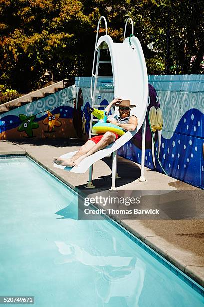 smiling man relaxing on waterside at outdoor pool - rutsche stock-fotos und bilder