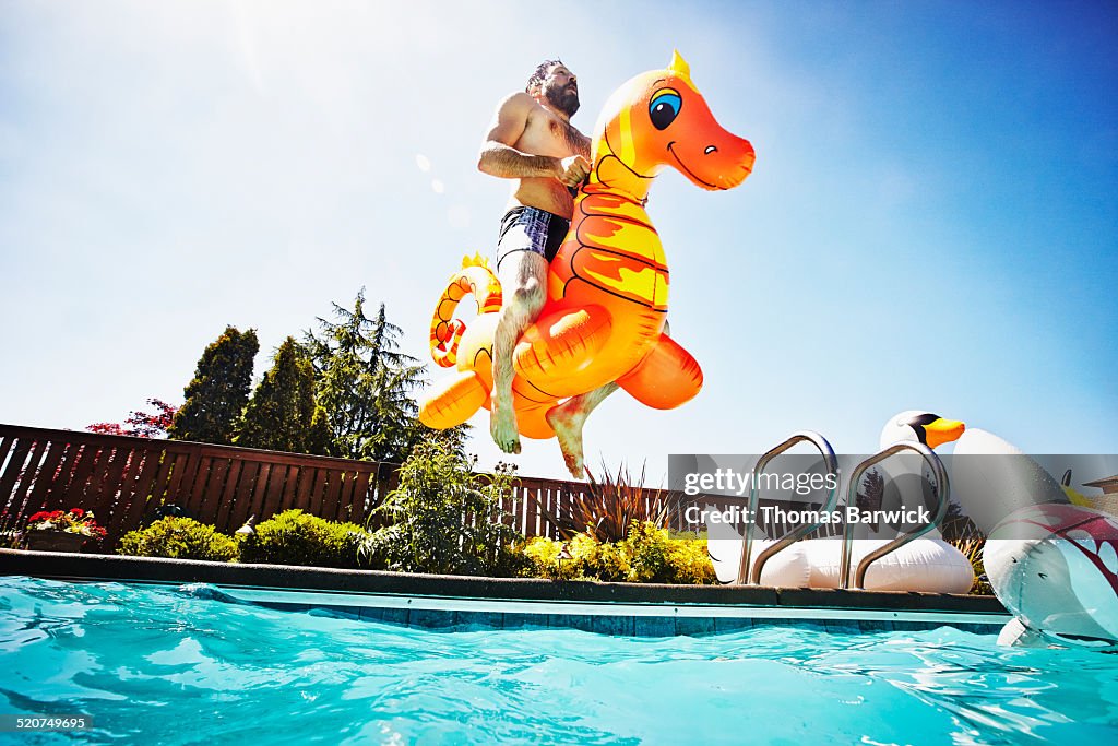 Man jumping into pool with inflatable pool toy