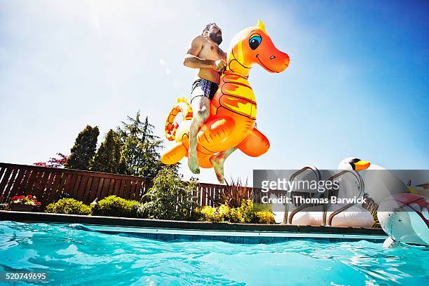 man jumping into pool with inflatable pool toy - saltare foto e immagini stock