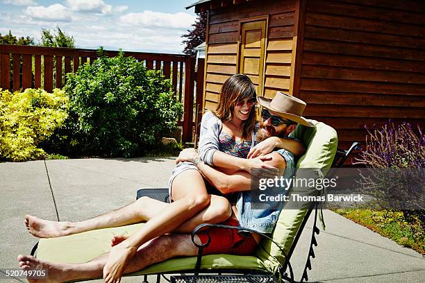 smiling woman sitting in mans lap on lounge chair - woman sitting on mans lap stockfoto's en -beelden