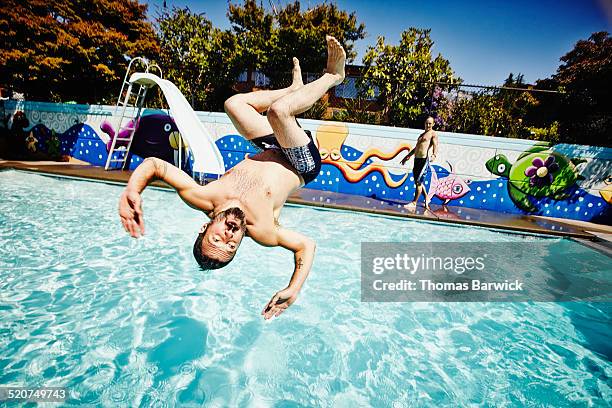 man doing backflip into outdoor swimming pool - salto de espalda fotografías e imágenes de stock