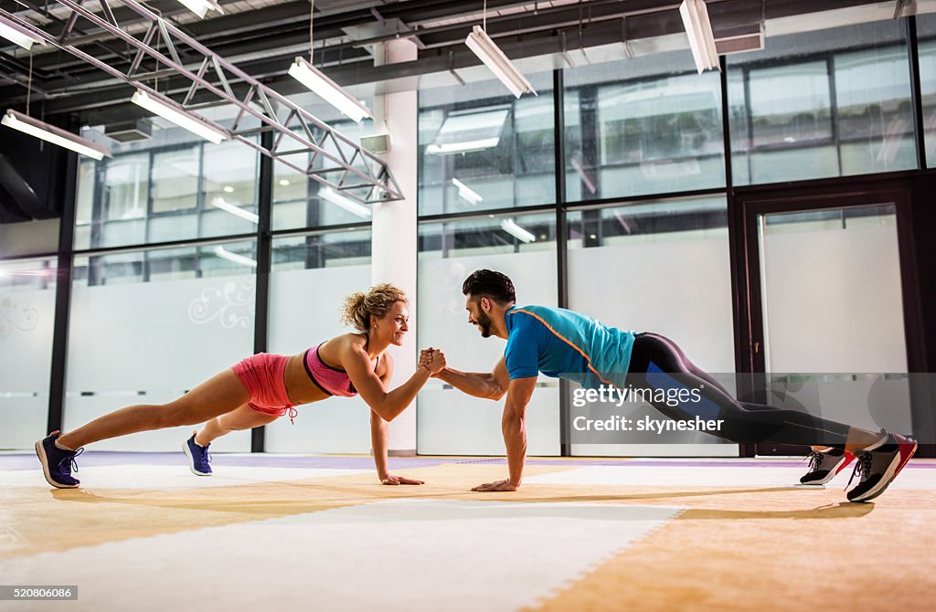 Smiling couple doing push-ups together in a gym.