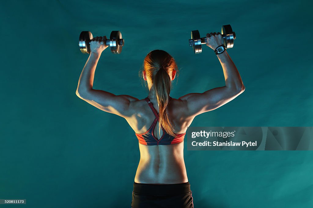 Girl training with dumbbells, back view, green ba