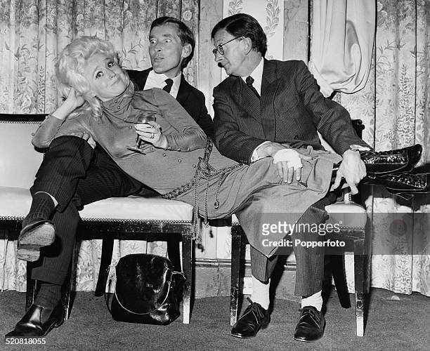 English comic actor and comedian Kenneth Williams and English comedy actor and musician Charles Hawtrey holding English actress Barbara Windsor at a...