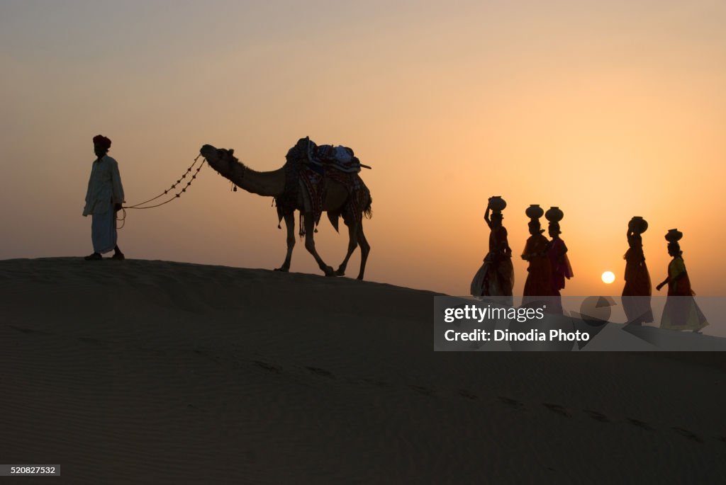 Men and woman with camel climbing up sand dune of khuhri, Jaisalmer, Rajasthan, India