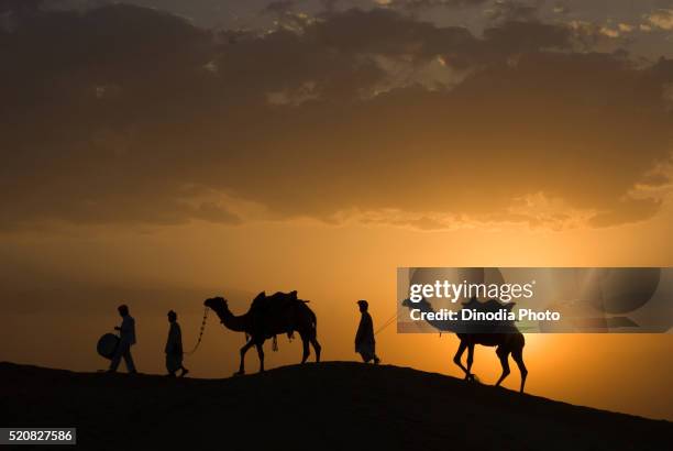 men with camels walking on sand dune of khuhri, jaisalmer, rajasthan, india - drummer silhouette stock pictures, royalty-free photos & images