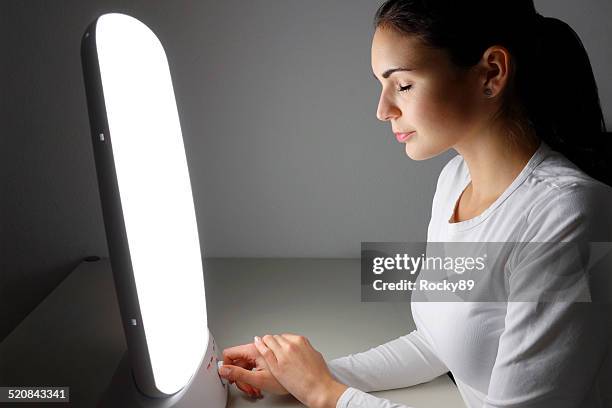 young woman administering a light therapy agains winter depression - seasonal affective disorder stock pictures, royalty-free photos & images