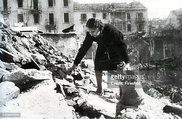 World War II-Italian Fascism 1944 1945-Bombing in Italy. A woman tries to recover some pieces of wood to burn in the midst of the rubble of a bombed...