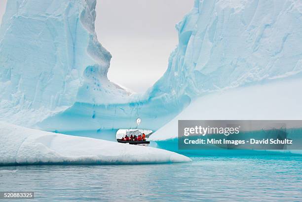 people in small inflatable zodiac rib boats passing towering sculpted icebergs on the calm water around small islands of the antarctic peninsula. - antarctica people stock pictures, royalty-free photos & images