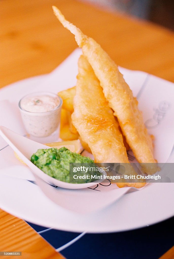 Traditional food, fried battered fish and chips, with mushy peas and tartar sauce on a plate.