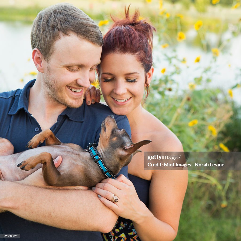 A couple playing with their small dog in the park.