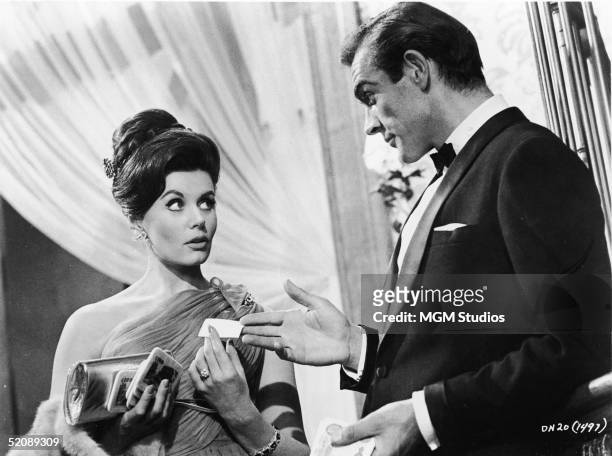 Scottish actor Sean Connery, as fictional secret agent James Bond, hands a business card to British actress Eunice Gayson in a scene from the film...