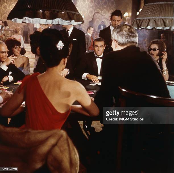 Scottish actor Sean Connery as fictional secret agent James Bond sits at a casino card table in a scene from the film 'Dr. No,' directed by Terence...