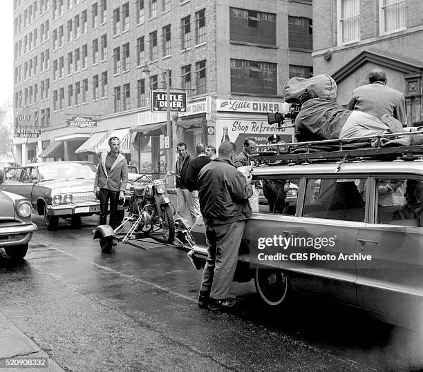 The film crew set up to shoot Julie Newmar from the top of a car as she is riding a motorcycle behind them, in "Route 66" episode: Give the Old Cat a...