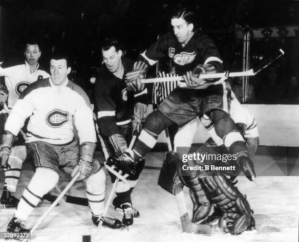 Gordie Howe of the Detroit Red Wings sneaks his stick past Montreal Canadiens Claude Provost , while Howe's teammate Ted Lindsay leaps into the air,...