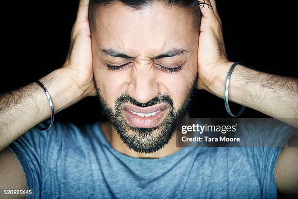 man blocking ears looking stressed - ohrenschmerzen stock-fotos und bilder