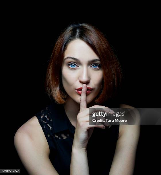 woman shushing with finger up to mouth - portrait on black background stock pictures, royalty-free photos & images