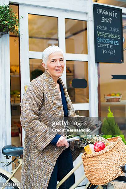 mature woman on bicycle in front of market - buying a bike bildbanksfoton och bilder